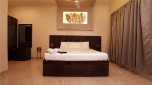 A hotel room with a large bed, a dark wooden headboard, a wall-mounted artwork, a flat-screen TV, and a large window with curtains. - Map Resort (Alibag)