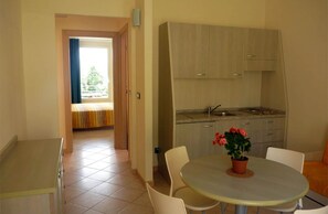 A compact kitchen with a dining area, a window with a view, and a potted plant on the table.