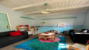 Una sala de estar con techo de madera, un sofá negro con un cojín rojo, una mesa de madera y una alfombra colorida.