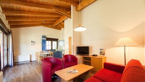 Una sala de estar acogedora con techo de madera, un televisor, un sofá rojo y un comedor al fondo.
