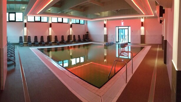 Una piscina interior moderna con una larga zona de asientos tipo banco y una barrera de vidrio.