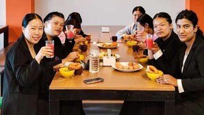 A group of people seated around a table with food and drinks, in a room with orange walls. - International Youth Hostel Inn (Pokhara)