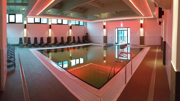 Une piscine intérieure moderne dotée d’un long banc et d’une paroi en verre.