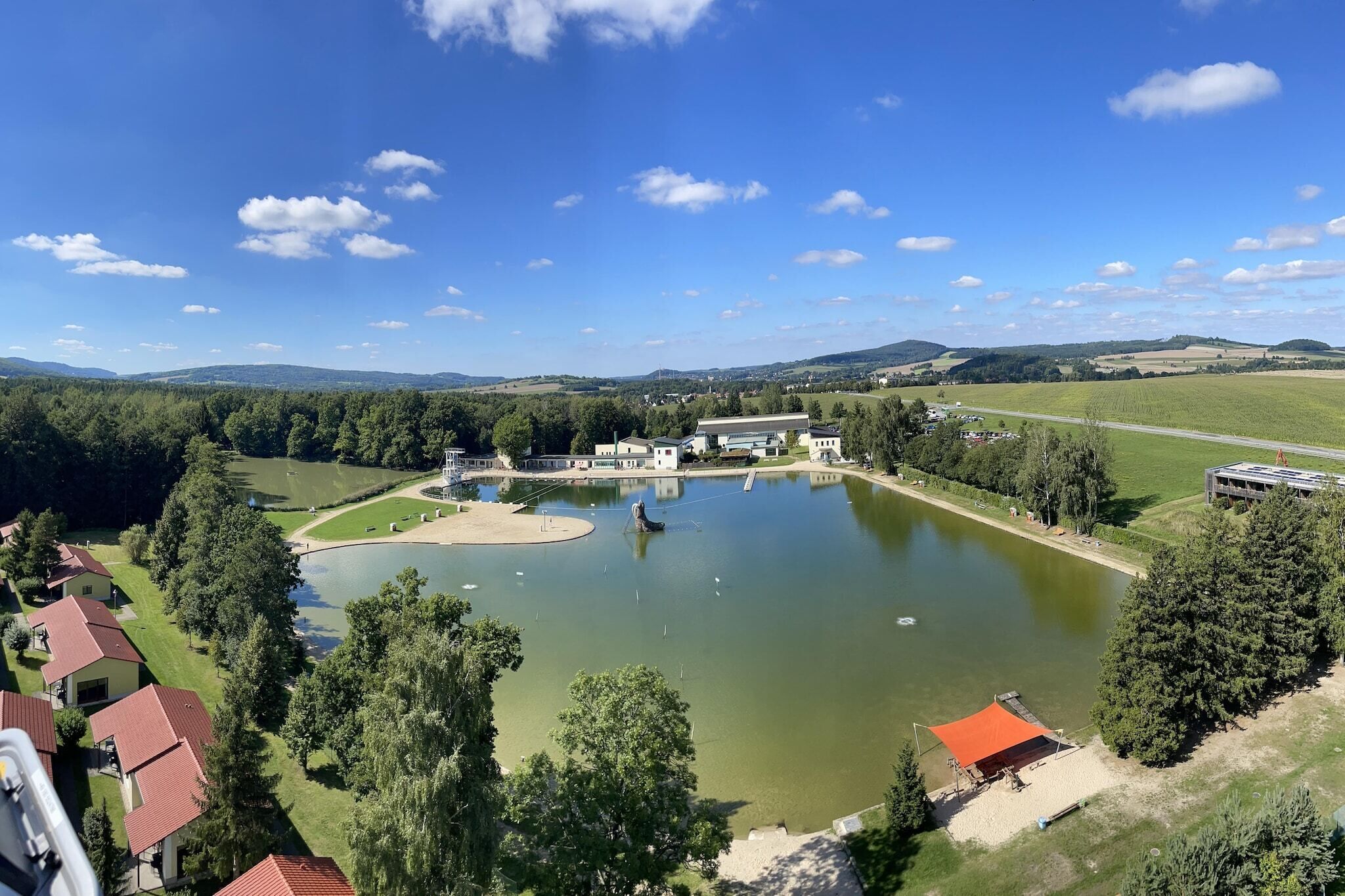 Una propietat a la vora d'un llac, amb un estany gran, una pista de tennis i un edifici amb teulada vermella.