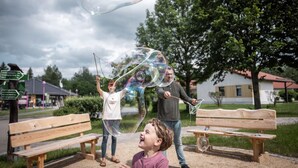 Un banc de parc, une personne tenant une baguette à bulles et une autre personne soufflant des bulles.