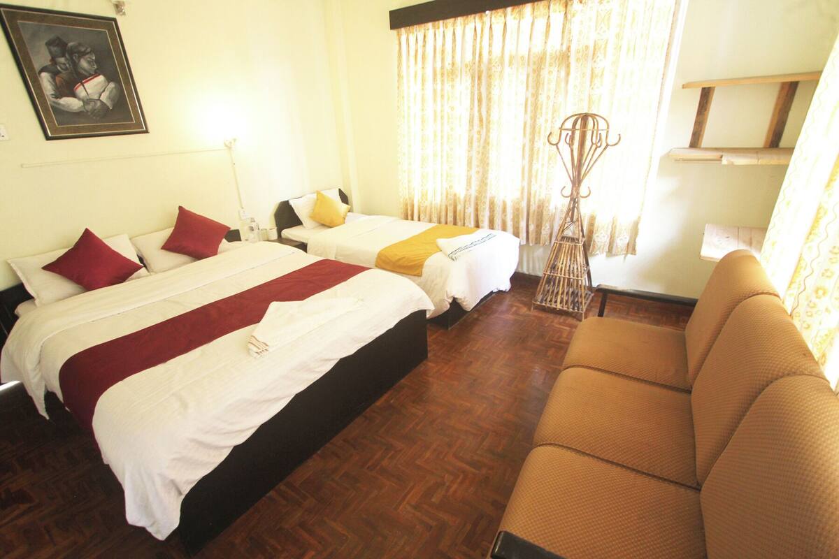 A hotel room with two beds, a sofa, a wooden floor, and a painting on the wall.