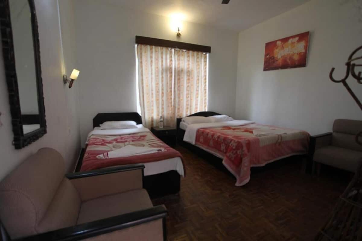 A hotel room with two single beds, a sofa, a chair, a mirror, and a curtain.