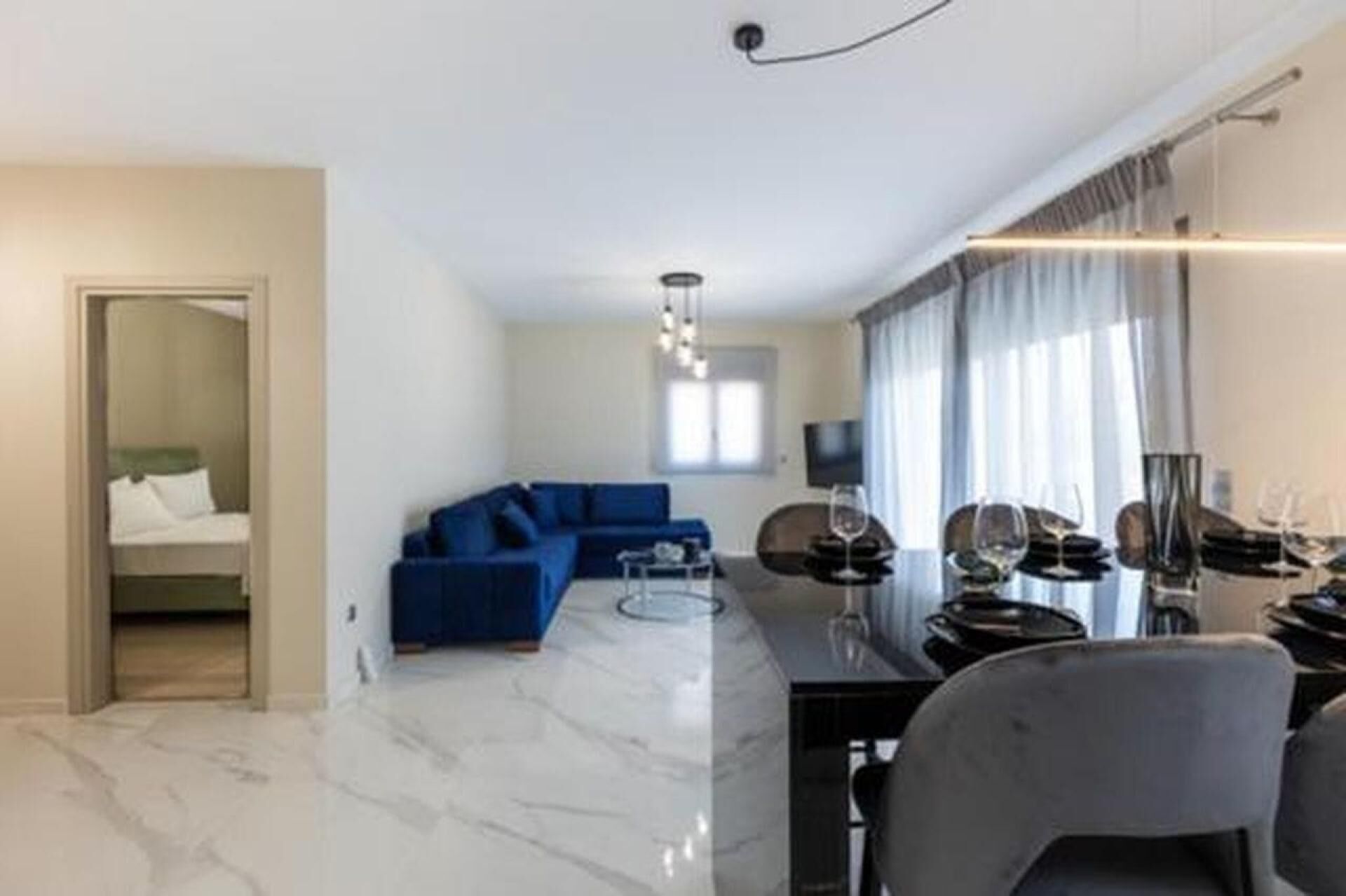 Uma sala de estar moderna com um sofá azul, uma área de jantar com mesa e cadeiras, e uma cozinha com fogão.