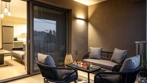 Ein moderner Balkon mit einer Couch, zwei Stühlen, einem Glastisch und Blick durch eine Schiebetür.