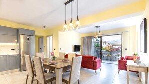 Een moderne keuken met een inbouwkoelkast, een eethoek met een houten tafel en stoelen, en een woonruimte met rode banken en een balkon met uitzicht.