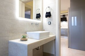 Een moderne badkamer met een wit wastafel, een glazen vaas met een plant en een handdoekhouder met een handdoek.