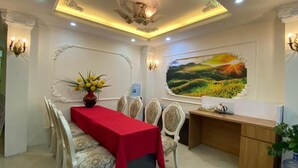 A dining area with a red table, white chairs, a vase with flowers, a painting on the wall, and a water dispenser. - Hanoi Milton Boutique Hotel  (Hanoi)