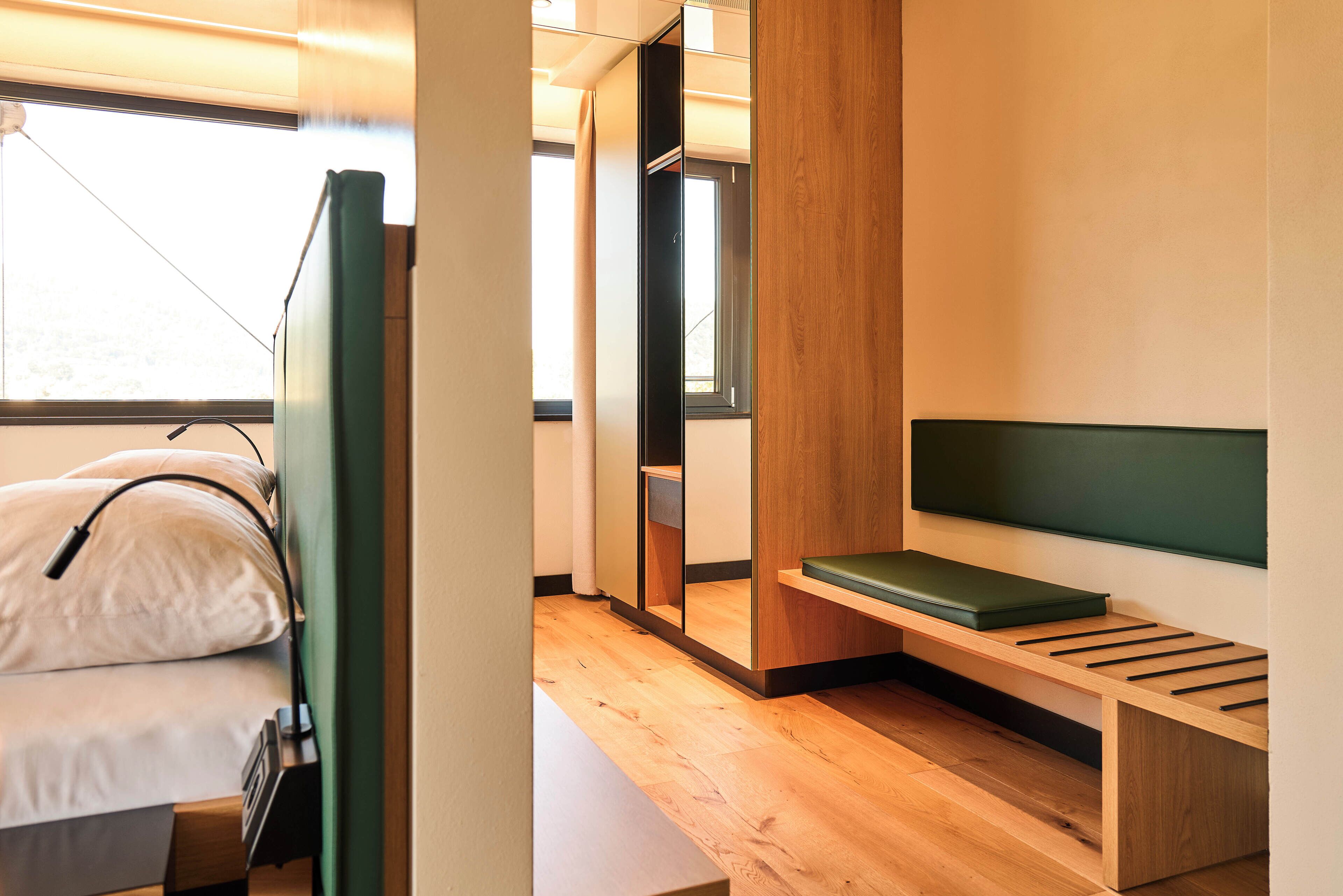 Une chambre moderne et compacte, équipée d’un lit, d’un banc et d’un miroir.