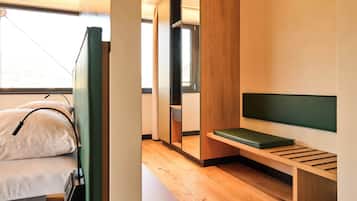 Een moderne, compacte kamer met een bed, een bankje en een spiegel.