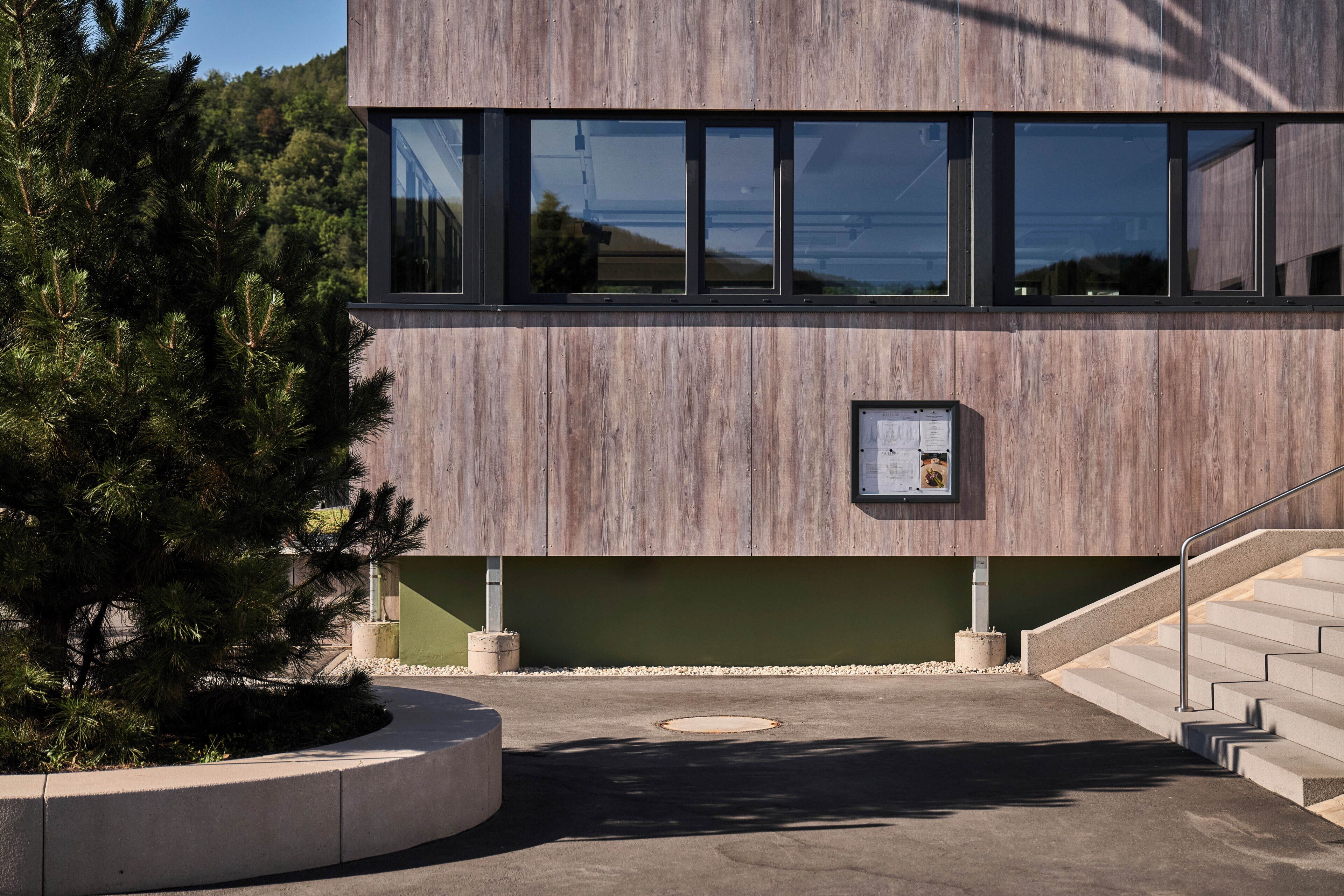 Un bâtiment moderne doté d’une façade en bois, d’un escalier et d’un espace paysager agrémenté d’un arbre.