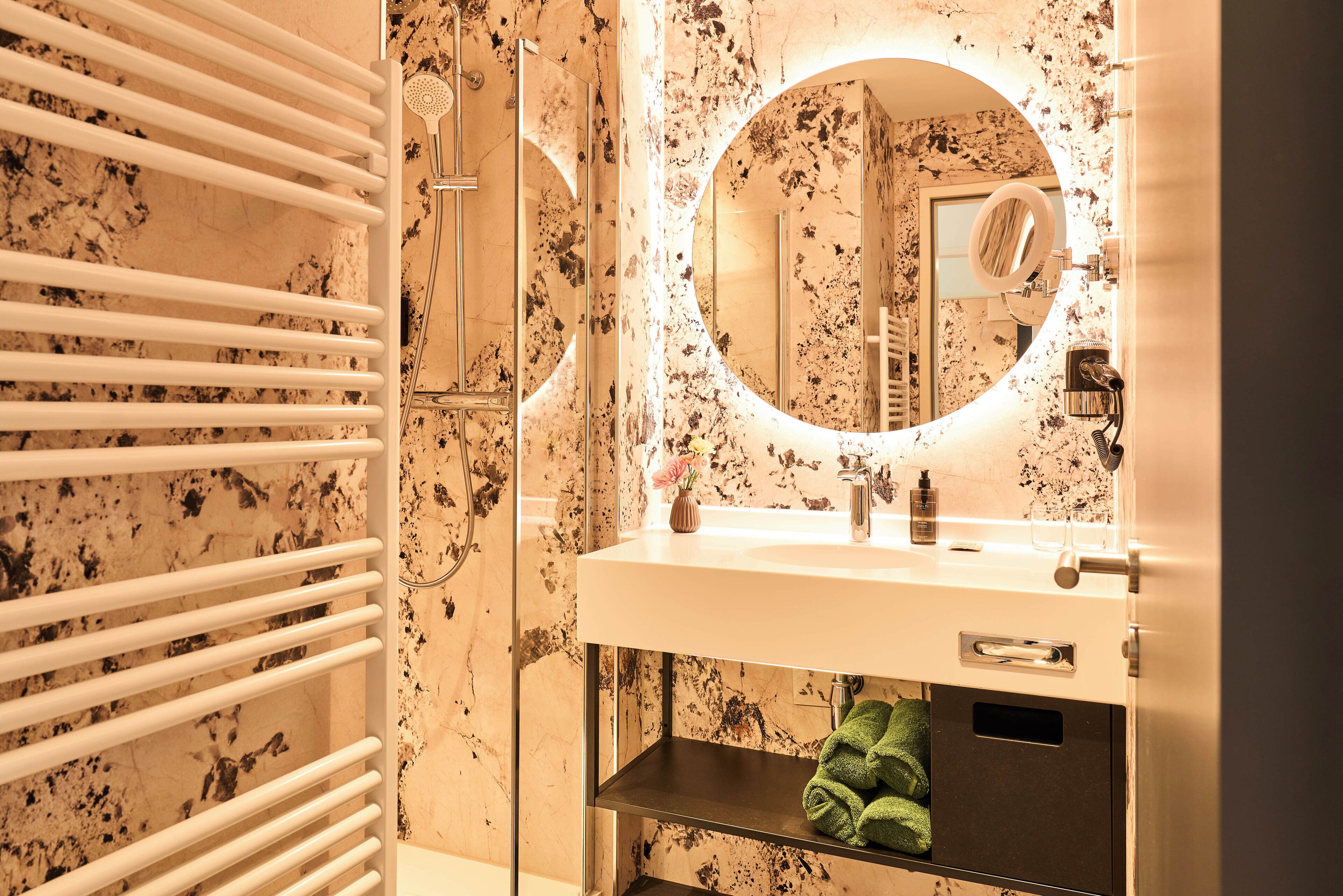 Un baño con pared de mármol, un lavabo blanco, un espejo y un perchero para toallas.