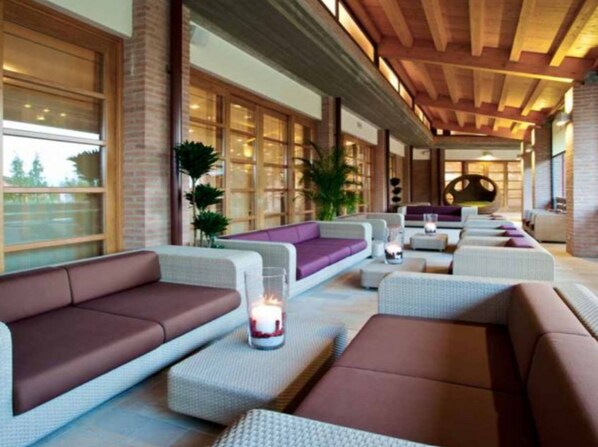 A modern lounge area with sofas and ottomans, large windows, and a wooden ceiling.