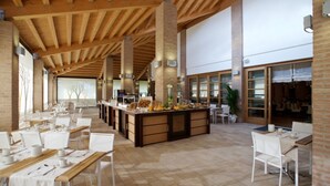 A spacious dining area with high ceilings and exposed wooden beams, featuring long tables set for dining and a central counter with food items. - Fabulous room in a modern resort (Lignano Sabbiadoro)