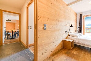 Ein Zimmer mit Holzwänden, einem Bett, einem kleinen Holzschemel und einem Tisch mit Stühlen.