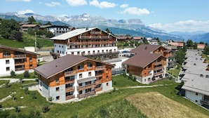 A cluster of wooden multi-story buildings with balconies, set against a backdrop of mountains.