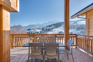 Eine Holzdielen-Terrasse mit Tisch und Stühlen mit Blick auf eine verschneite Landschaft und Berge.
