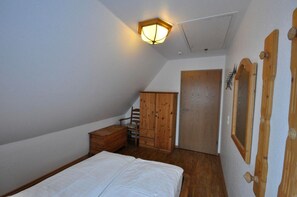 Ein Schlafzimmer mit schrägen Wänden, einem Holzschrank, einer Kommode aus Holz, einem Bett und einer Tür.