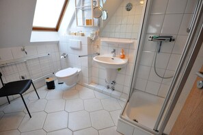 Ein modernes Badezimmer mit Toilette, Waschbecken, Dusche und einem Sessel.