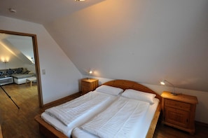 Ein Schlafzimmer mit einem hölzernen Bett, zwei Nachttischen, einem Spiegel und Blick auf einen Wohnbereich.