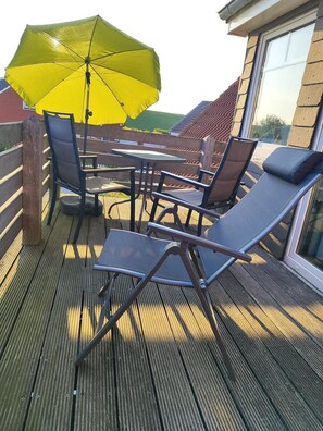 Ein Sitzbereich im Freien mit Tisch und Stühlen, einem gelben Sonnenschirm und Blick auf die Landschaft.