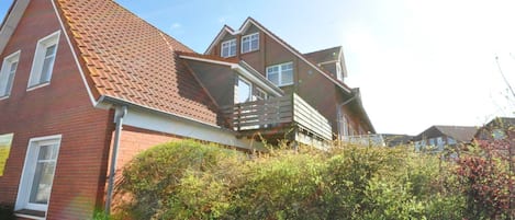 Une maison à deux étages avec une façade en briques rouges, un toit en pente et un balcon.