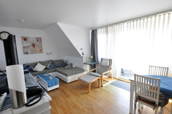 A modern living room with a sofa, a small table, a chair, and a dining table with chairs.
