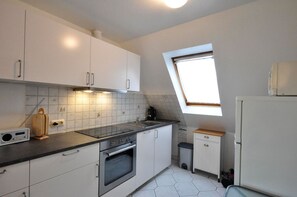 A compact kitchen with white cabinets, a black countertop, a built-in oven, a small trash bin, and a window providing natural light.