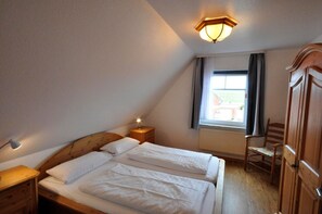 A bedroom with a wooden bed, bedside tables, a nightstand, a chair, and a window with curtains.