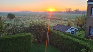 Un atardecer sobre un paisaje rural con una casa pequeña y un campo.