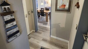 Un pasillo que conduce a un comedor con una mesa y sillas de madera, una lámpara colgante y un cuadro en la pared.