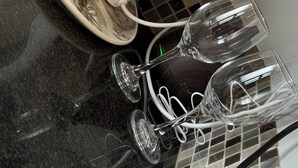 Una encimera de cocina con una cafetera, azúcar en bolsa y varias copas de vino.