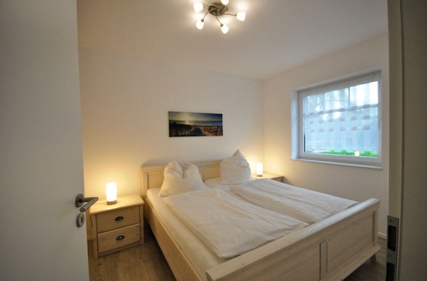 Une chambre à coucher avec un lit, des tables de chevet, une commode, une fenêtre et un tableau au mur.