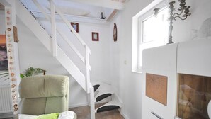 Een kamer met een witte trap, een groene stoel, een houten kast en een raam met een kandelaar.
