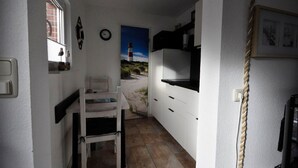 Een smalle keuken met witte kastjes, een kleine eettafel en een schilderij van een vuurtoren aan de muur.