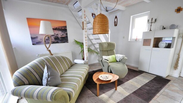 Een woonkamer met een gestreept bankje, een groene fauteuil, een klein houten tafeltje en een hangende rotanlamp.