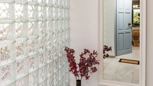 Un couloir avec une cloison en verre, un vase rempli de fleurs rouges et un miroir qui reflète une porte et un coin repas.