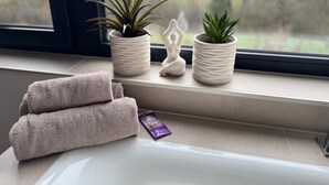 Een badkamer met een raam, twee potplanten, een handdoek en een zeepstaafje.