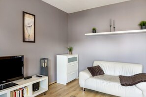 Un salon moderne avec un téléviseur à écran plat, un canapé blanc et une bibliothèque.