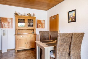 Un coin repas avec des chaises en osier, une table en bois, un meuble avec des portes en verre et des œuvres d’art accrochées au mur.