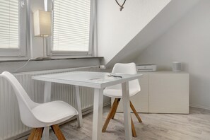 A modern room with a glass table, white chairs, a white cabinet, and a radiator.