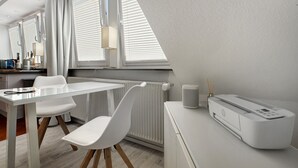 Ein modernes Zimmer mit Glastisch, weißen Stühlen, Heizkörper, Lampe und einem HP-Drucker.