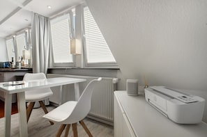 Une pièce moderne avec une table en verre, des chaises blanches, un radiateur, une lampe et une imprimante HP.
