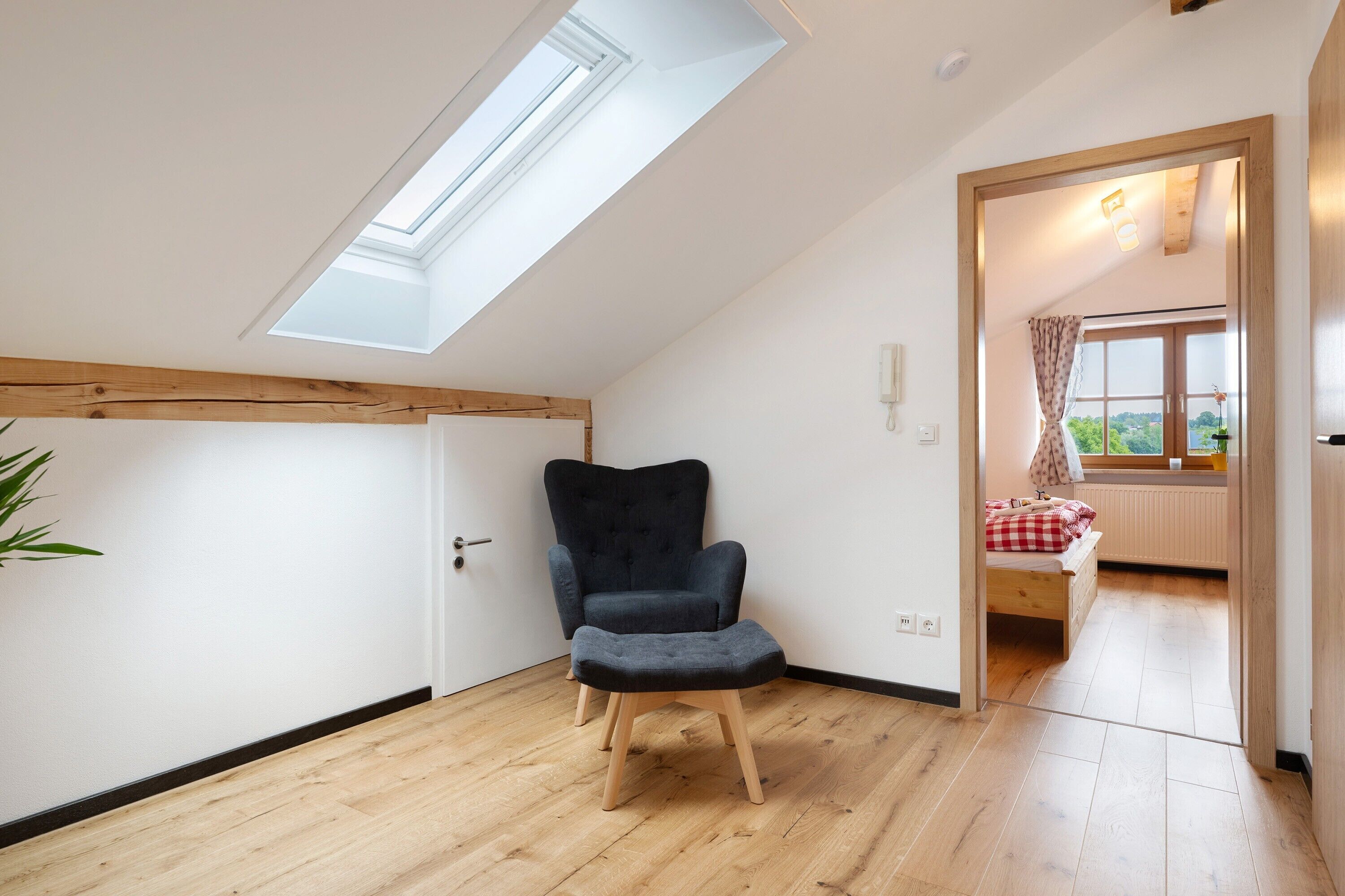 A room with a skylight, a dark armchair, a wooden floor, and a bed with a window view.