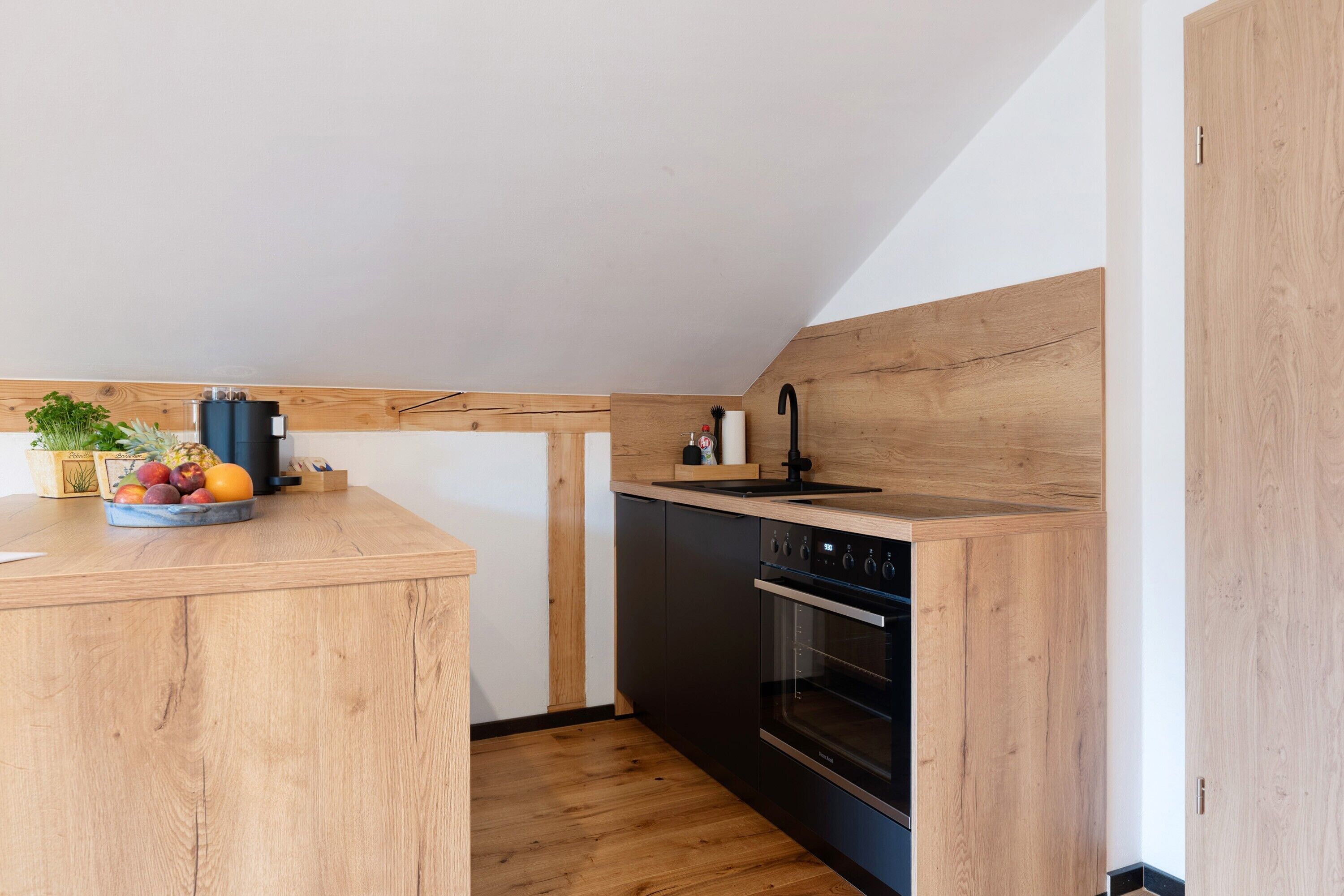 A modern kitchen with wooden cabinetry, a built-in oven, and a fruit bowl on the counter.