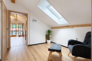 A room with a skylight, a potted plant, a grey chair, and a wooden floor.